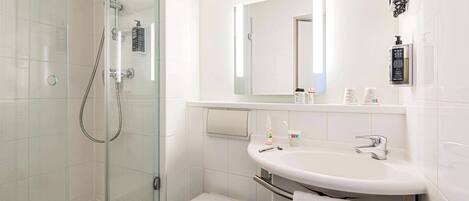 Un baño moderno con ducha de vidrio, inodoro blanco, lavamanos con toallero y espejo.