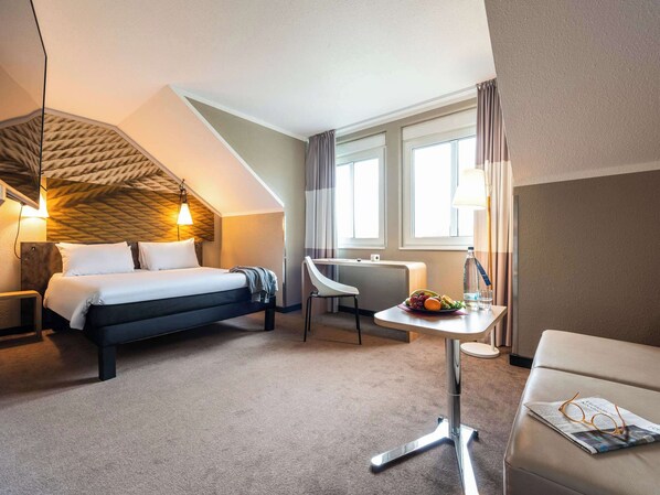 Une chambre d’hôtel équipée d’un lit, d’un bureau, d’une chaise et d’une petite table sur laquelle se trouvent un panier de fruits et des verres.