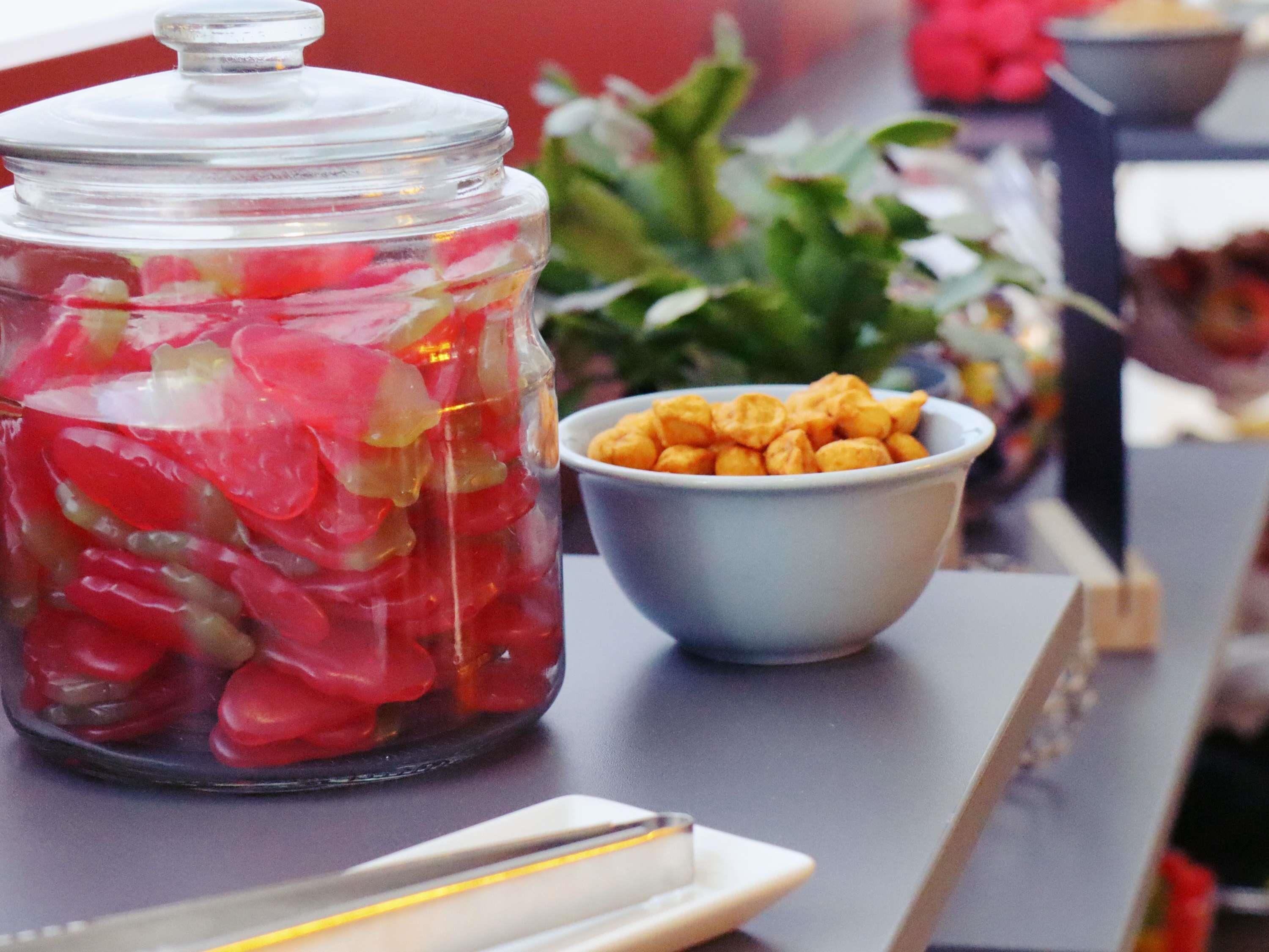 A glass jar filled with red and yellow items, a bowl of snacks, and a white plate on a table.