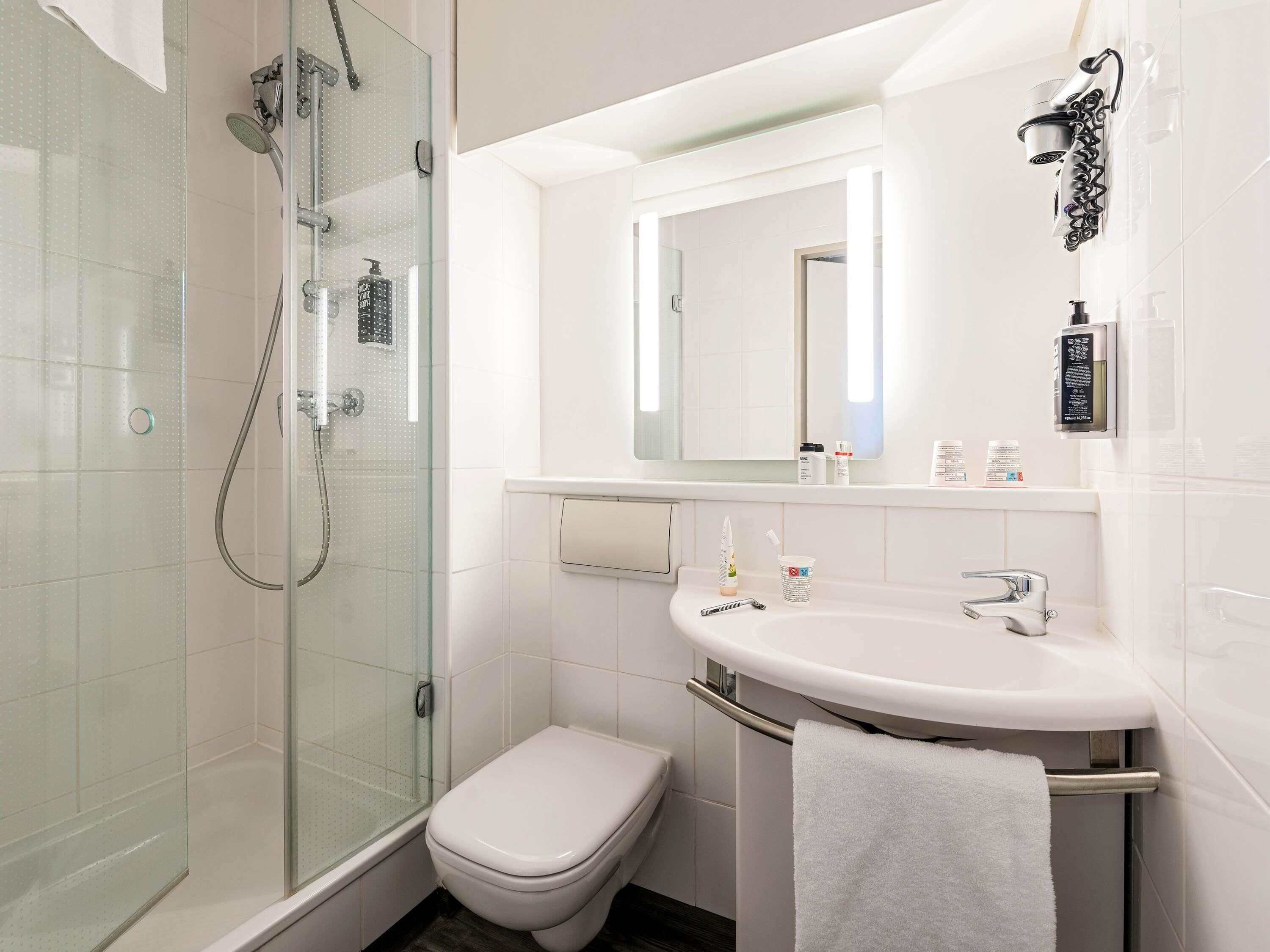Un baño moderno con cabina de ducha de vidrio, inodoro blanco, lavamanos con toallero y espejo.