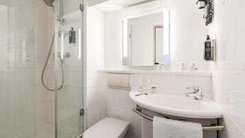 A modern bathroom with a glass shower enclosure, a white toilet, a sink with a towel rack, and a mirror.