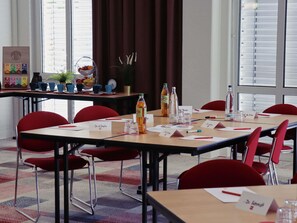A conference room with tables, chairs, nameplates, and various items like cups, bottles, and a clock. - ibis Regensburg City (Regensburg)