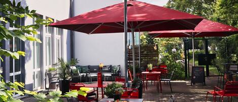 Une terrasse extérieure avec des tables et des chaises rouges, un lampadaire et un sol en briques.