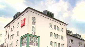 A multi-story building with a flat facade, multiple windows, and red signage indicating it is an ibis hotel.