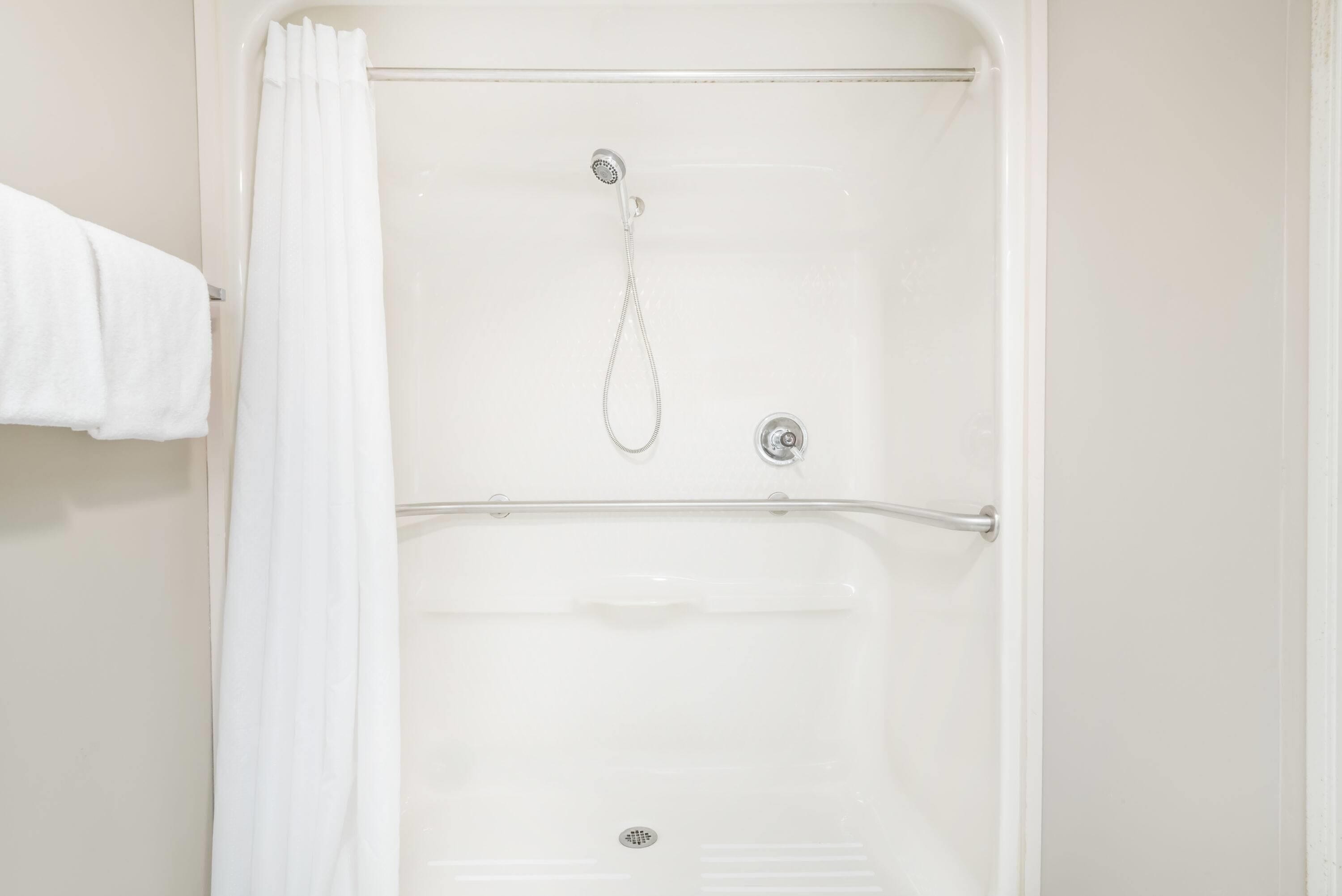 Un box de ducha blanco con cabezal, baranda y panel de control.