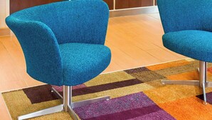 Un hall d’hôtel moderne avec deux fauteuils bleus, un comptoir d’accueil en bois et un tapis aux couleurs vives.