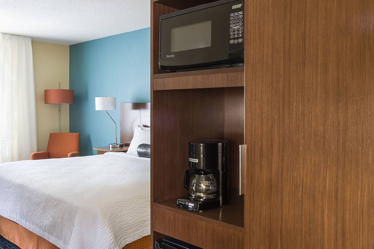 A hotel room with a bed, a microwave, a coffee maker, and a mini-fridge.