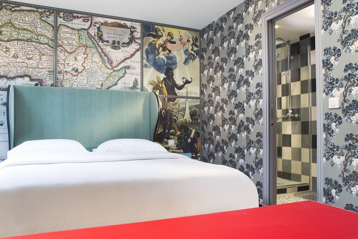Hotellihuone, jossa on suuri sänky, seinällä kartta ja ruutukuviollinen suihkuovi.