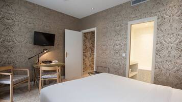 Una habitación de hotel con cama, escritorio con silla, televisor montado en la pared y puerta que da a un baño.