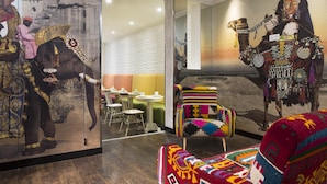 Una habitación con un mural de un elefante y un hombre, un sillón colorido y una alfombra estampada.