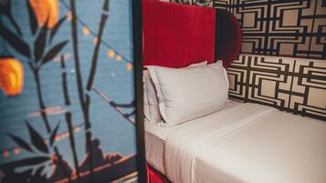 Una cama con ropa blanca y un cabecero rojo, frente a una pared con diseño.