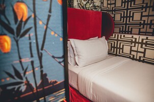A bed with white bedding and a red headboard, set against a patterned wall.