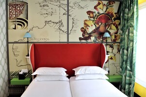 A hotel room with a red headboard, white bedding, a map on the wall, and a green nightstand.