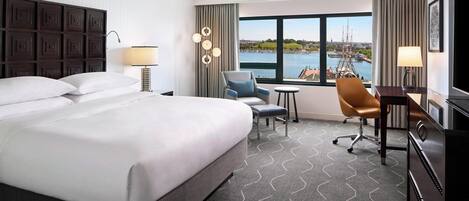 Een hotelkamer met een groot bed, een bureau, een stoel en uitzicht op een wateroppervlak.