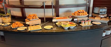 A buffet counter with various food items, including pastries, fruits, and condiments.