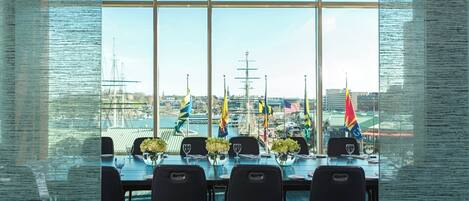 A conference room with a large window overlooking a harbor with ships and flags.