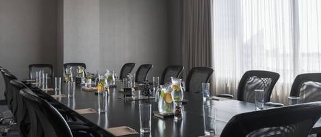 A conference room with a long table, black chairs, and a pitcher of water with lemon slices.
