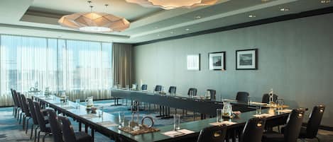 Un salón de conferencias con una larga mesa, sillas y modernas lámparas.