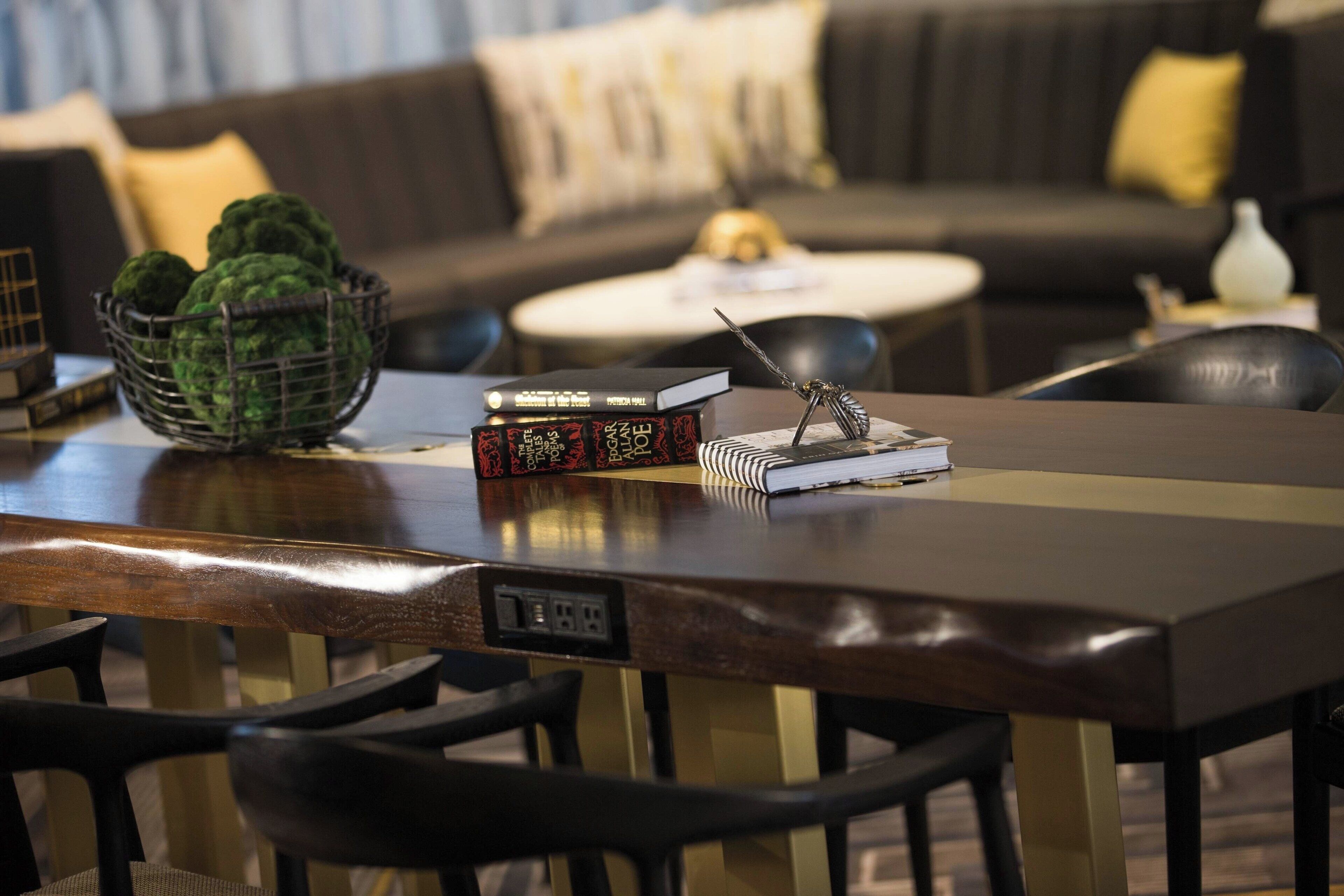 A dining area with a wooden table, chairs, a basket of green apples, books, and a decorative metal sculpture.
