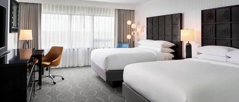 Une chambre d’hôtel avec deux lits, un bureau, une chaise et un téléviseur.