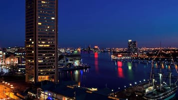 Une vue nocturne d’une ville, avec un gratte-ciel imposant en premier plan, un port de plaisance avec des bateaux et un pont en arrière-plan.