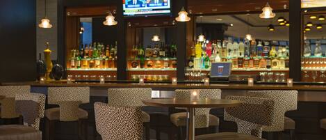 A bar area with patterned chairs, a television screen, and a variety of bottles.