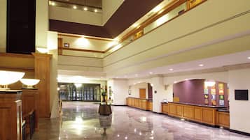 A spacious lobby with a marble floor, wooden reception desk, and a large vase with flowers.