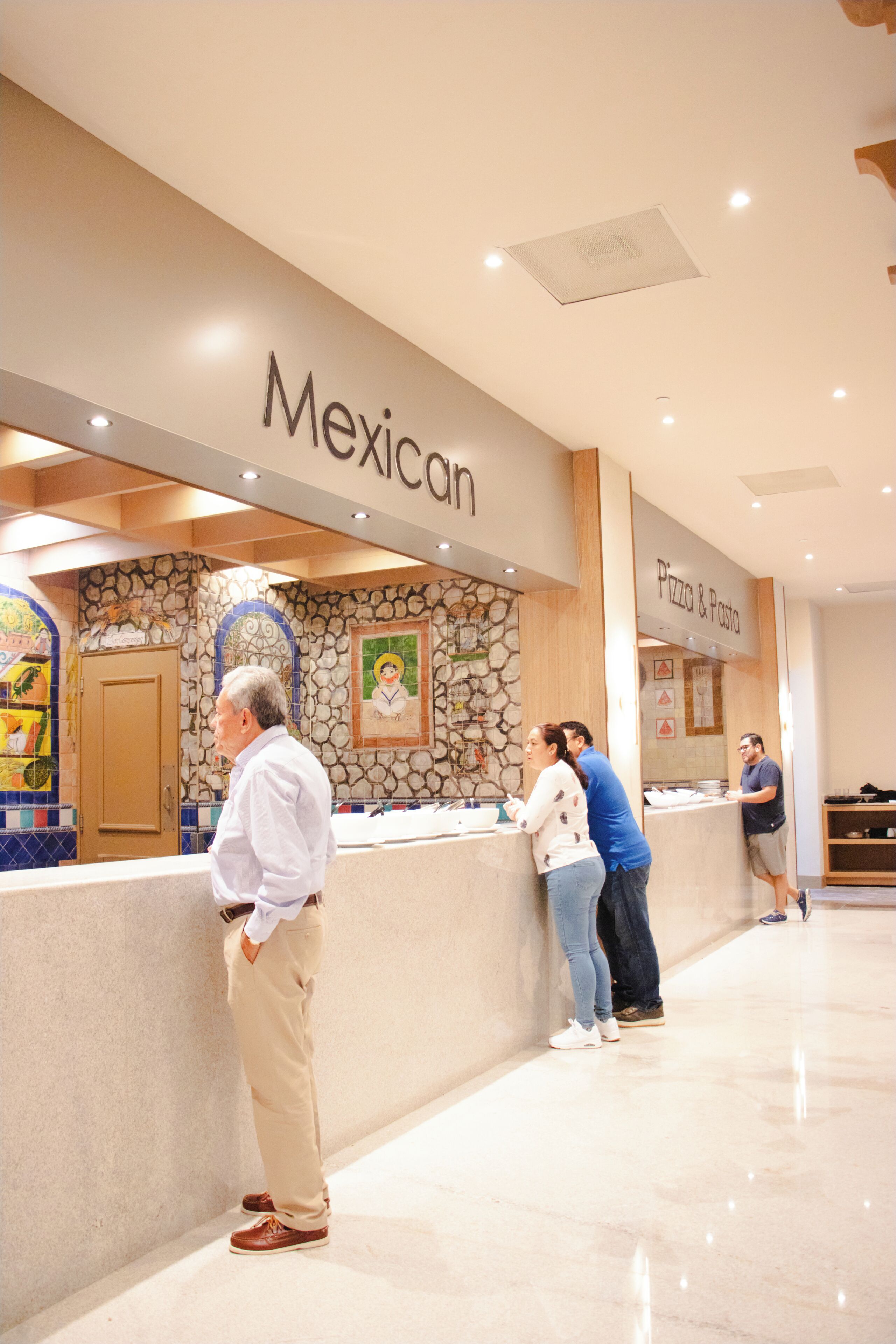 A reception area with a 'Mexican' sign, a stone wall with a mural, and a 'Pizza & Pasta' counter.