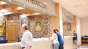 A reception area with a 'Mexican' sign, a stone wall with a mural, and a 'Pizza & Pasta' counter.