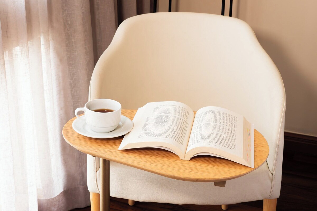 A chair with a wooden tray holding a cup of coffee and an open book.