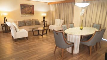 A hotel room with a wooden floor, a round dining table with chairs, a sofa, a coffee table, and two lamps.