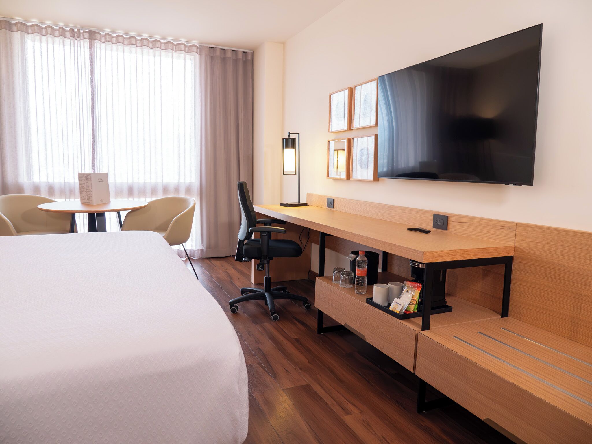 Habitación de hotel con una cama grande, un escritorio con una silla, un televisor y una ventana con cortinas.