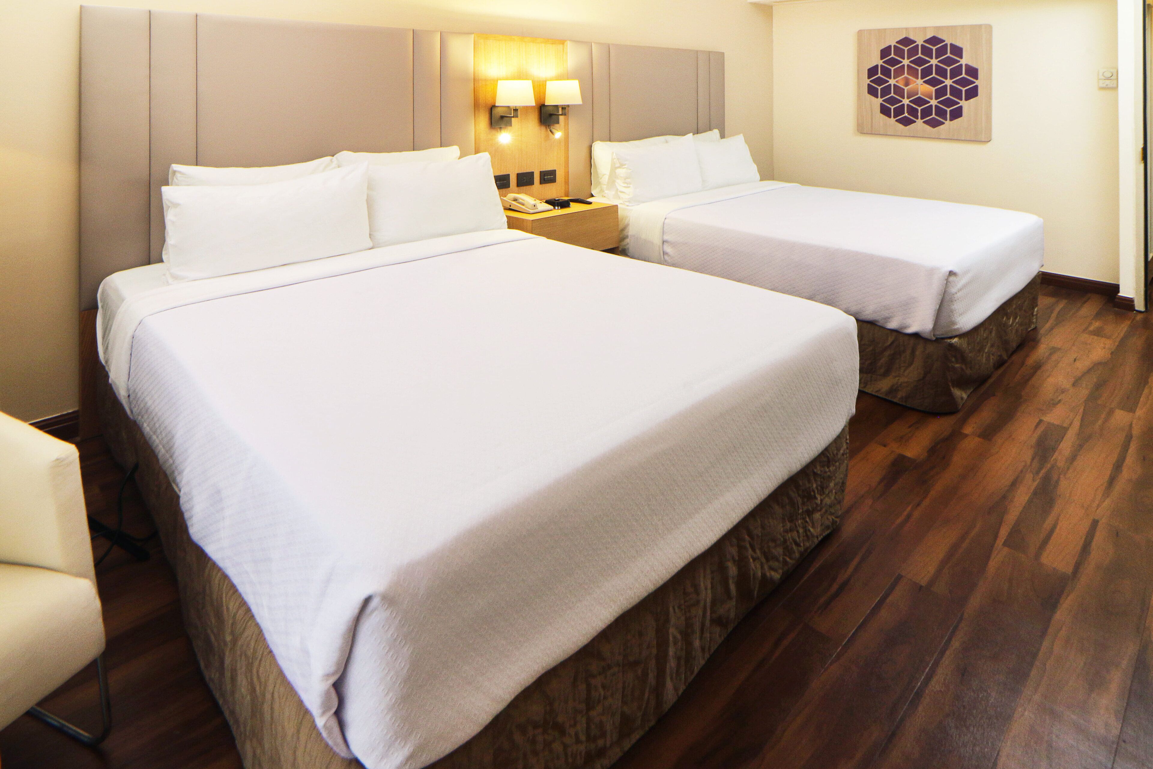 A hotel room with two beds, a nightstand with a phone, and a wall-mounted light fixture.