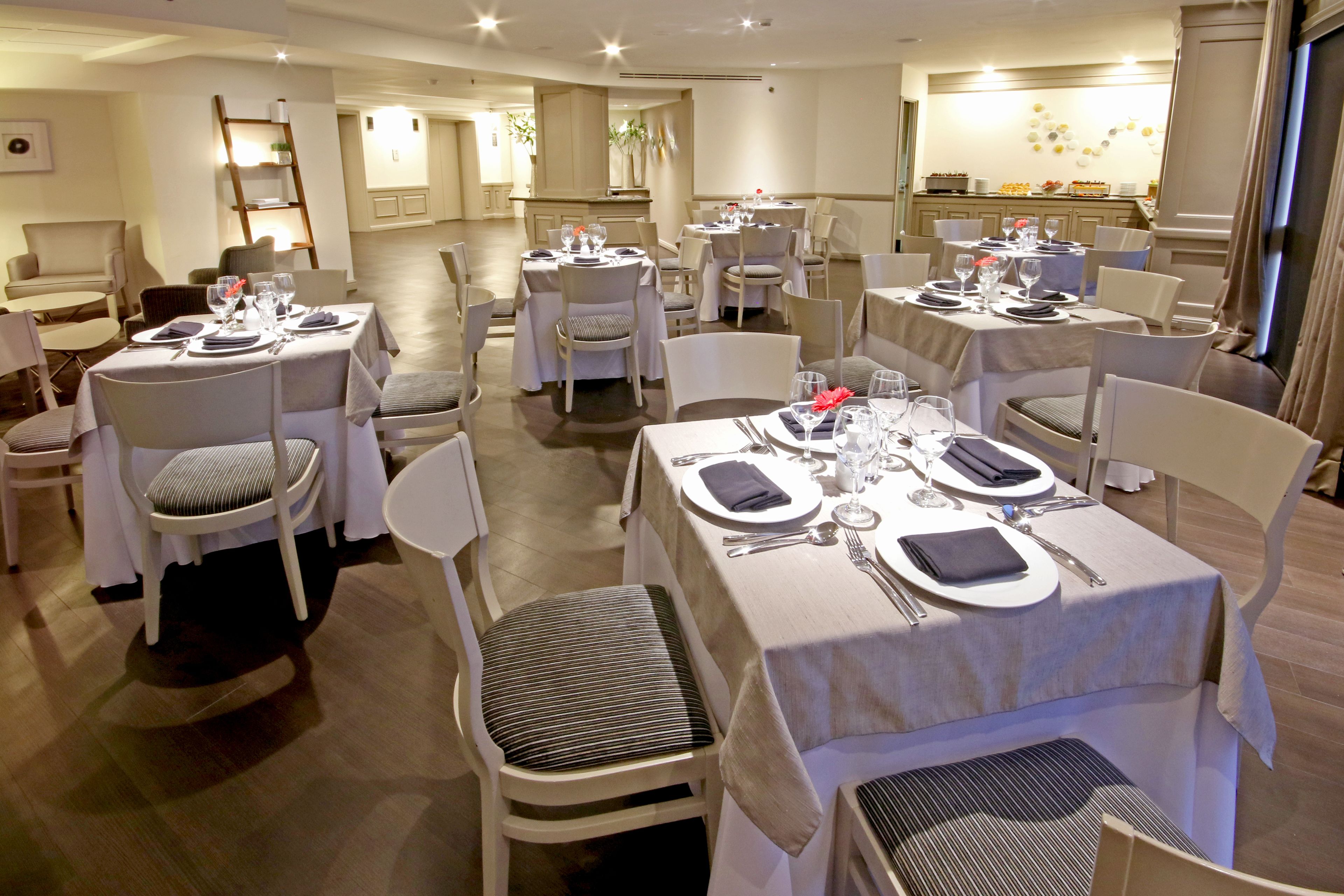 A dining area with multiple tables set for guests, each with white tablecloths, chairs, and neatly arranged tableware.