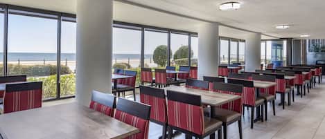 A spacious dining area with high tables and chairs, large windows offering a view of the beach and ocean.