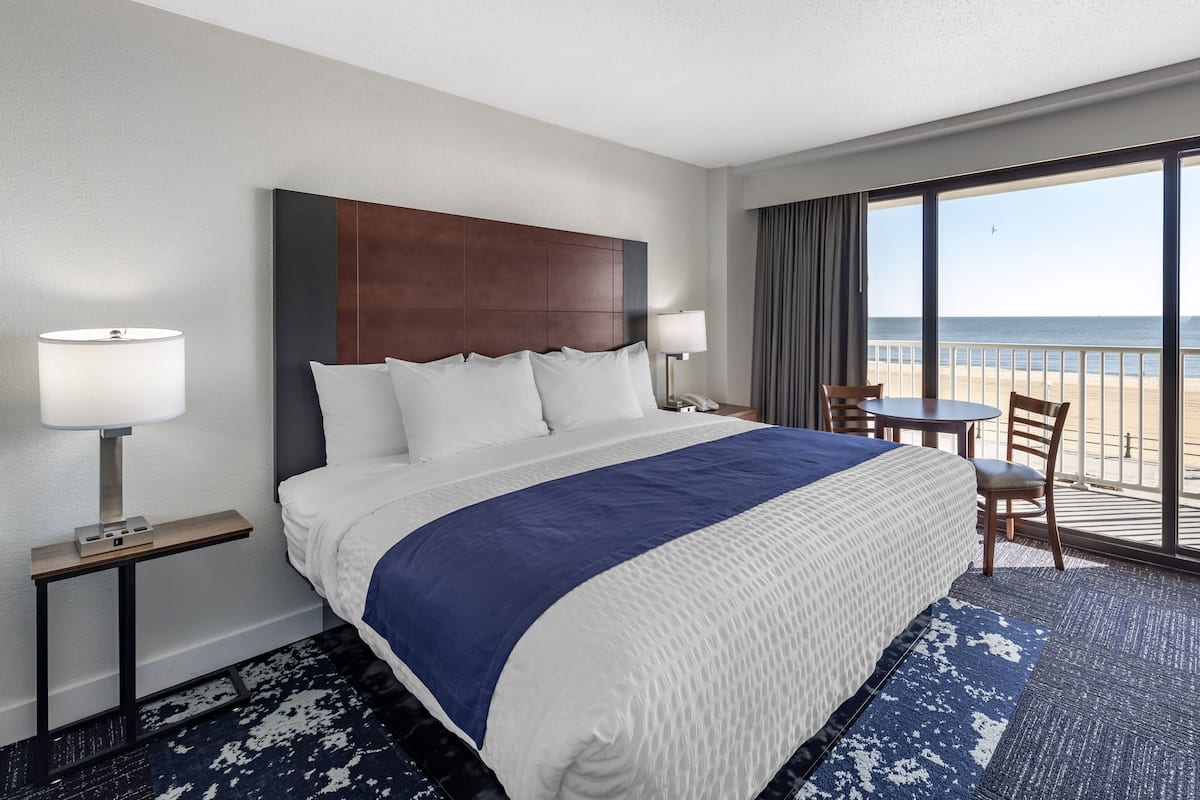 Habitación de hotel con una cama grande, un escritorio, una silla y vista a la playa.