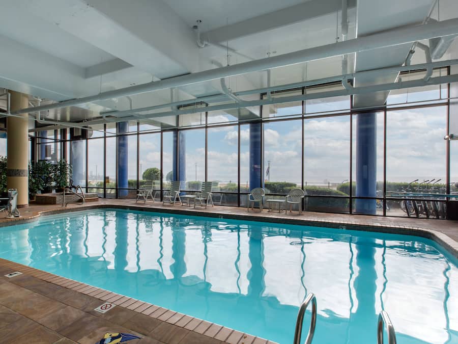 An indoor swimming pool with clear glass walls, a tiled floor, and a view of the sky and clouds.