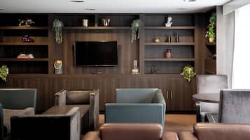 A modern living room with a large flat-screen TV, dark wood shelving with decorative items, and comfortable seating.