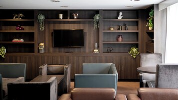 A modern living room with a large flat-screen TV, dark wood shelving with decorative items, and comfortable seating.