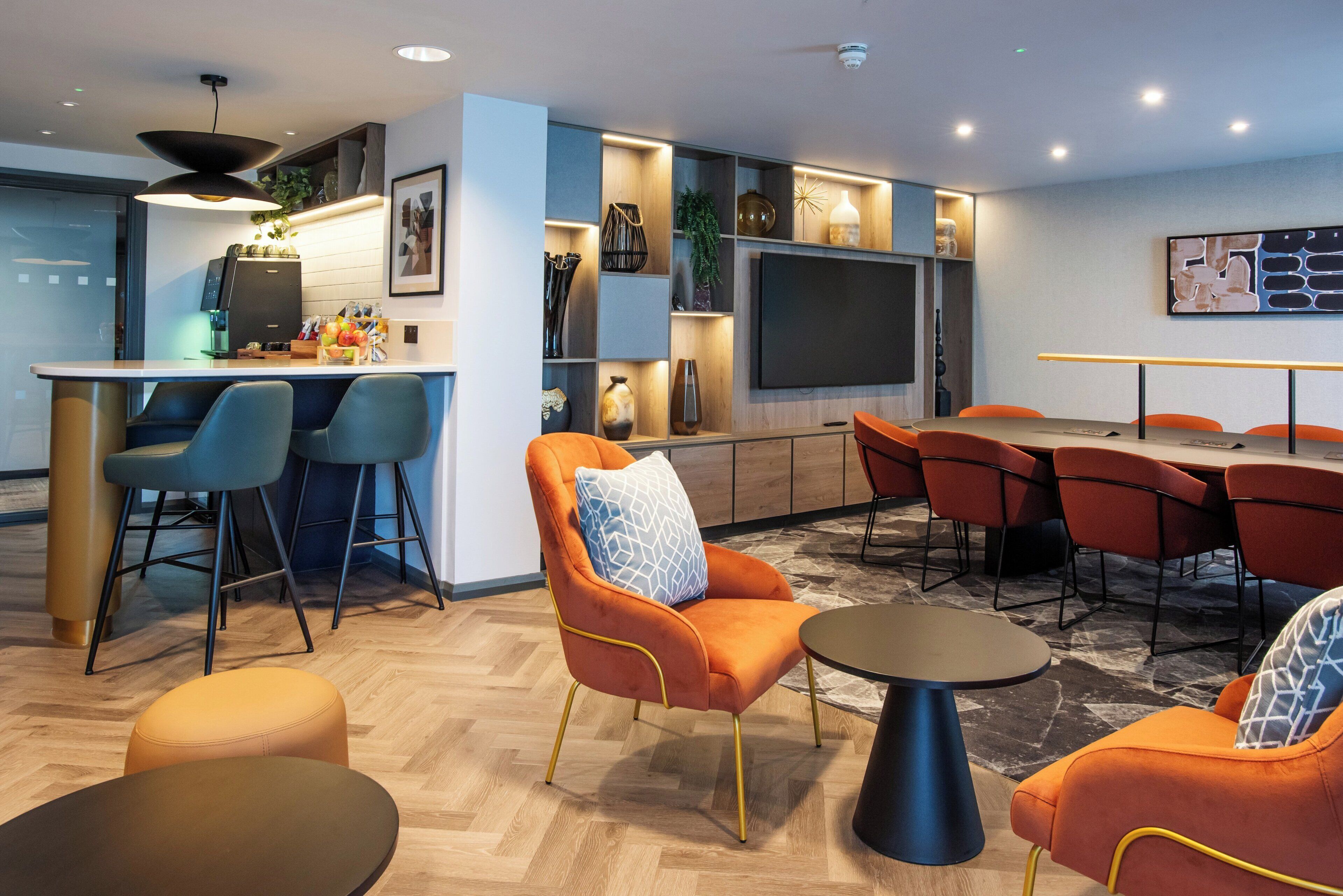 A modern lounge area with a bar, seating, a flat-screen TV, and a coffee machine.