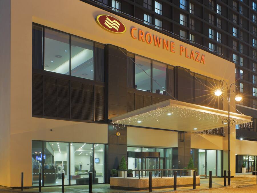 A hotel entrance with a sign reading "CROWNE PLAZA" and a covered outdoor area with lights.