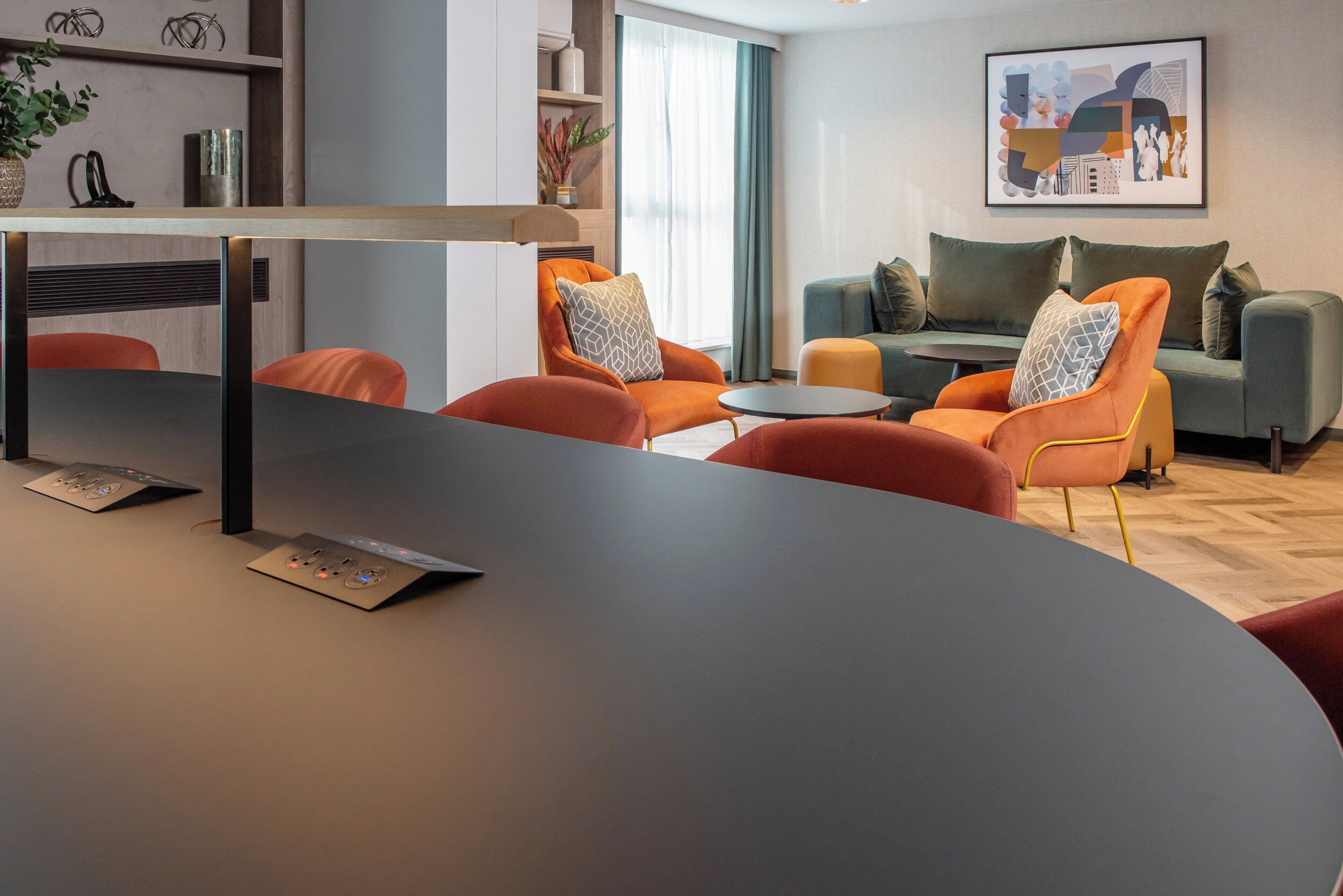 A modern living room with a central table, orange chairs, a grey sofa, and a coffee table.