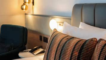 A hotel room with a bed, a bedside table with a lamp, a telephone, and a chair.