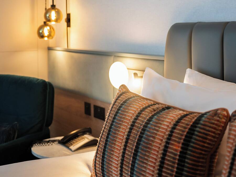 A hotel room with a bed, a bedside table with a lamp, a telephone, and a chair.