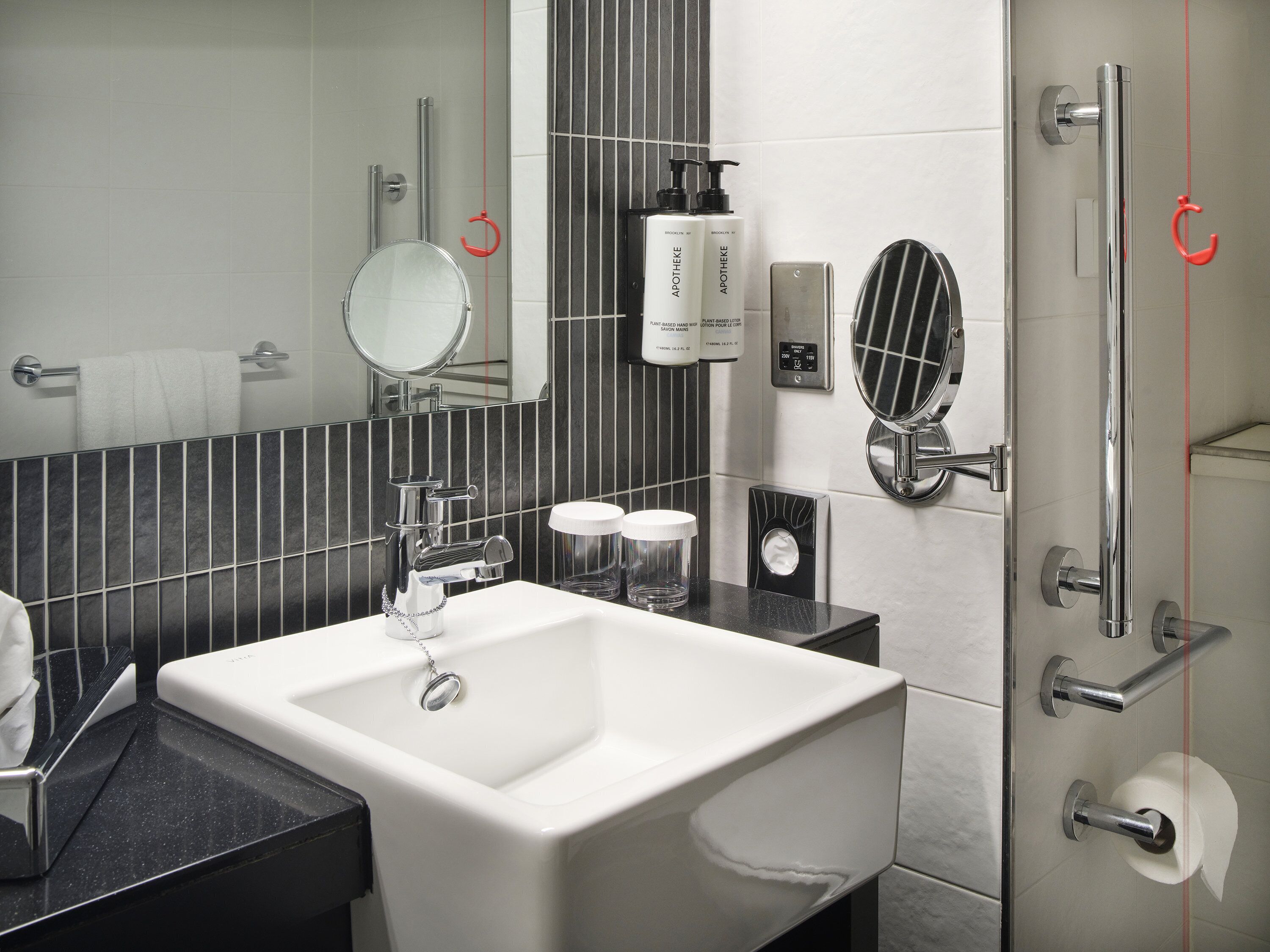 A modern bathroom with a white sink, a mirror, a towel rack, a shower with a glass door, and toiletries on the wall.