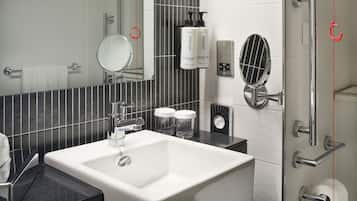 A modern bathroom with a white sink, a mirror, a towel rack, a shower with a glass door, and toiletries on the wall.