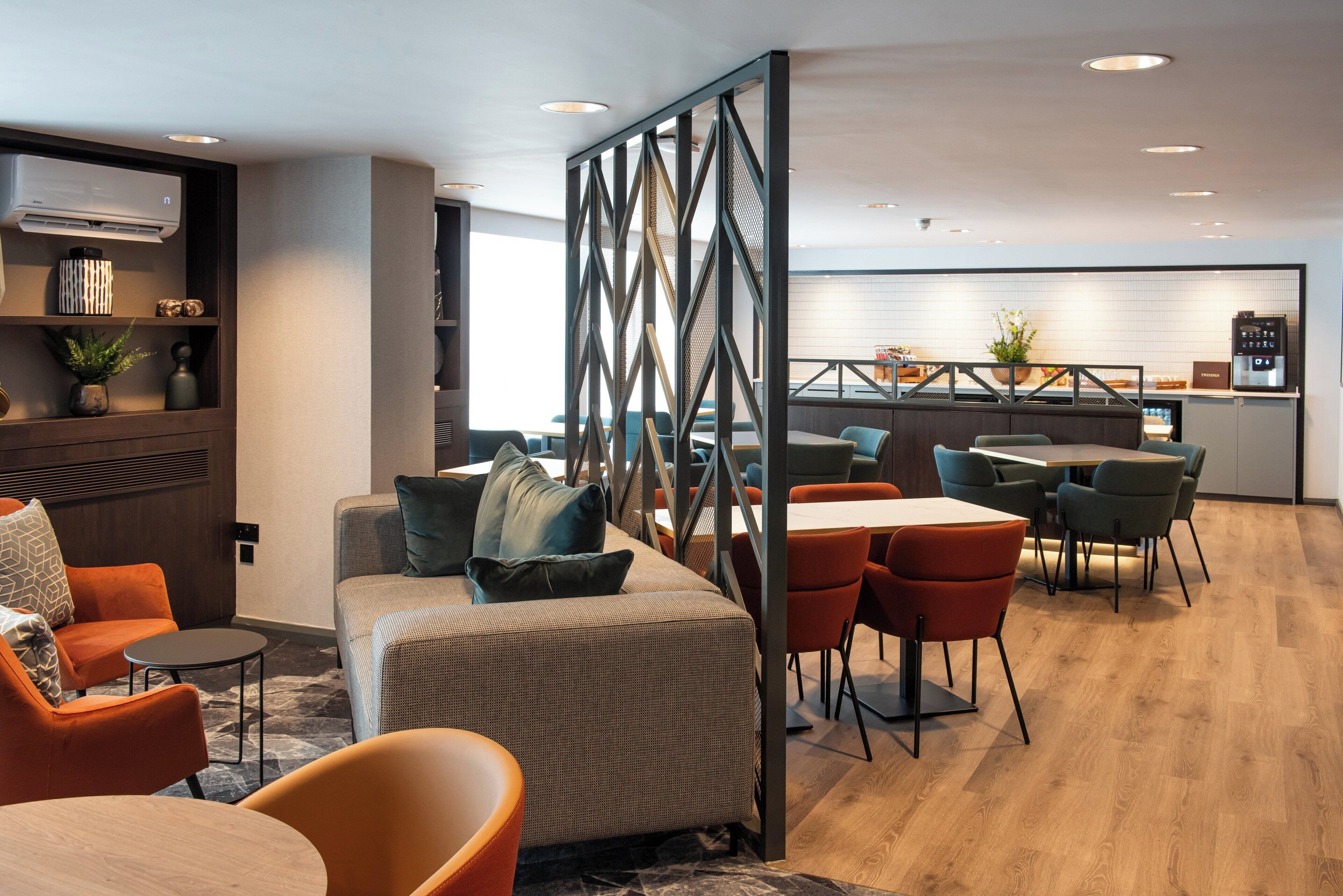 A modern hotel lobby with a seating area, a kitchen in the background, and a view of the city.
