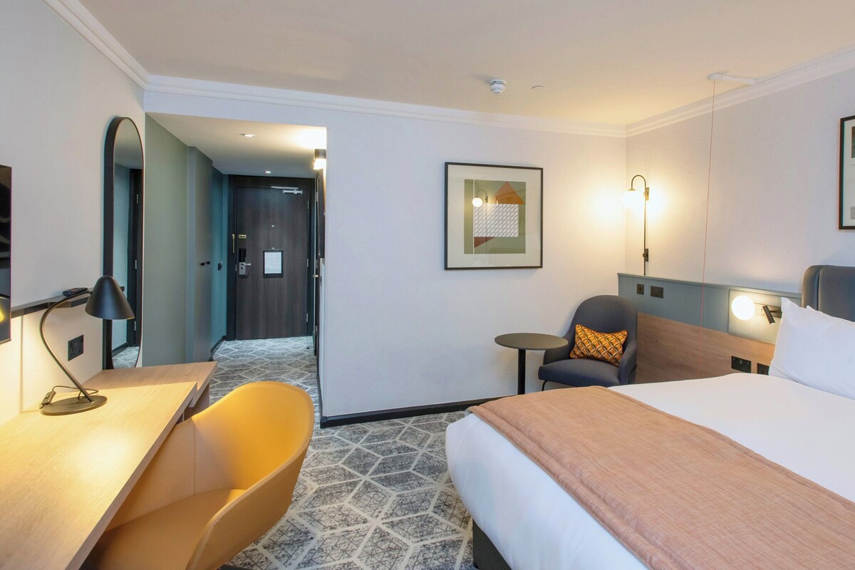 A hotel room with a bed, a desk, a chair, and a small table.