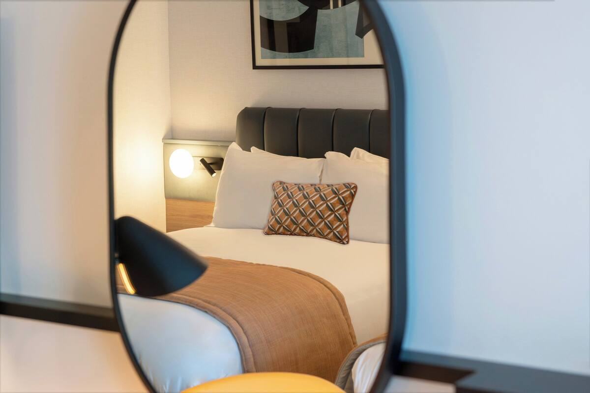 Een hotelkamer met een bed, kussens, een nachtkastje en een lamp.