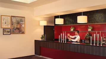 A hotel reception area with a red counter, multiple drink dispensers, and two hanging pendant lights.